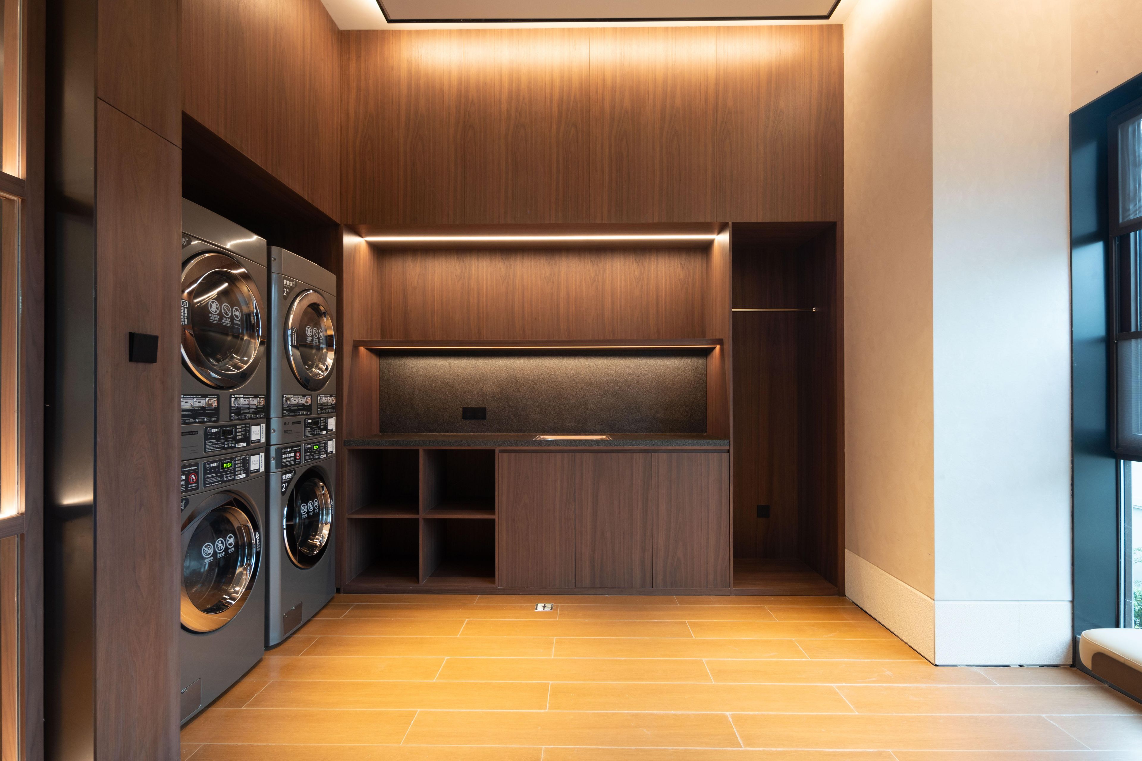 A modern laundry room with built-in washers and dryers, wooden paneling, and a bench.