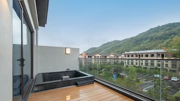 Uma varanda com piso de madeira, uma banheira de hidromassagem e vista para um estacionamento e edifícios ao fundo.