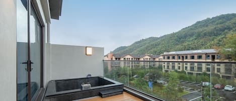 A balcony with a wooden floor, a hot tub, and a view of a parking lot and buildings in the background.