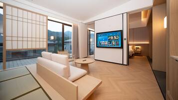 Quarto de hotel moderno com sofá, mesa redonda, televisão na parede e vista para o exterior.