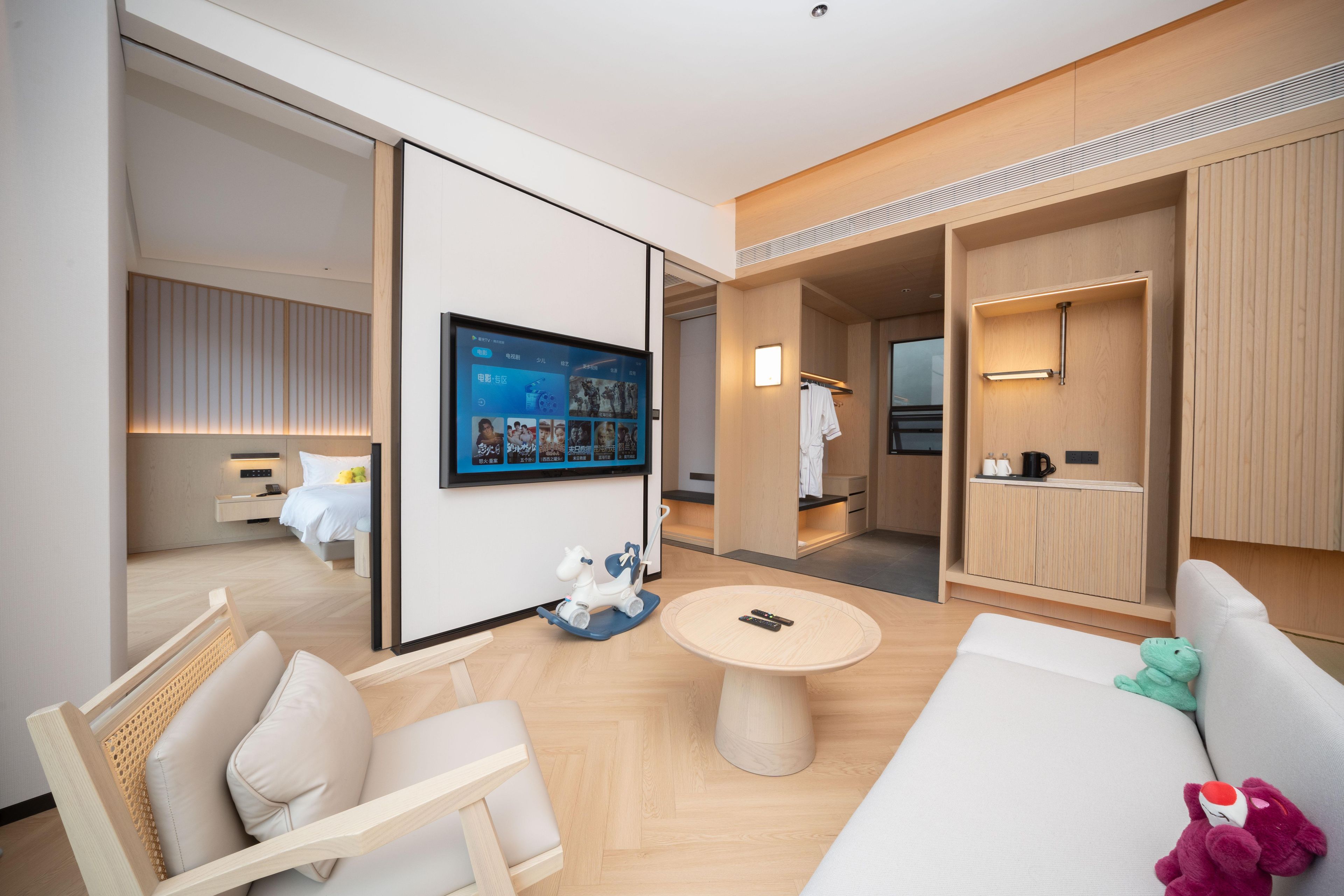 A modern hotel room with a sofa, a small round table, a mounted TV, and a wardrobe.