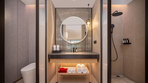 A modern bathroom with a round mirror, a sink, a shower, and neatly folded towels on a shelf. - Madison Hot Spring Hotel Jian Wugong Mountain (Ji'an)