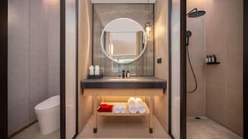 A modern bathroom with a round mirror, a sink, a shower, and neatly folded towels on a shelf.