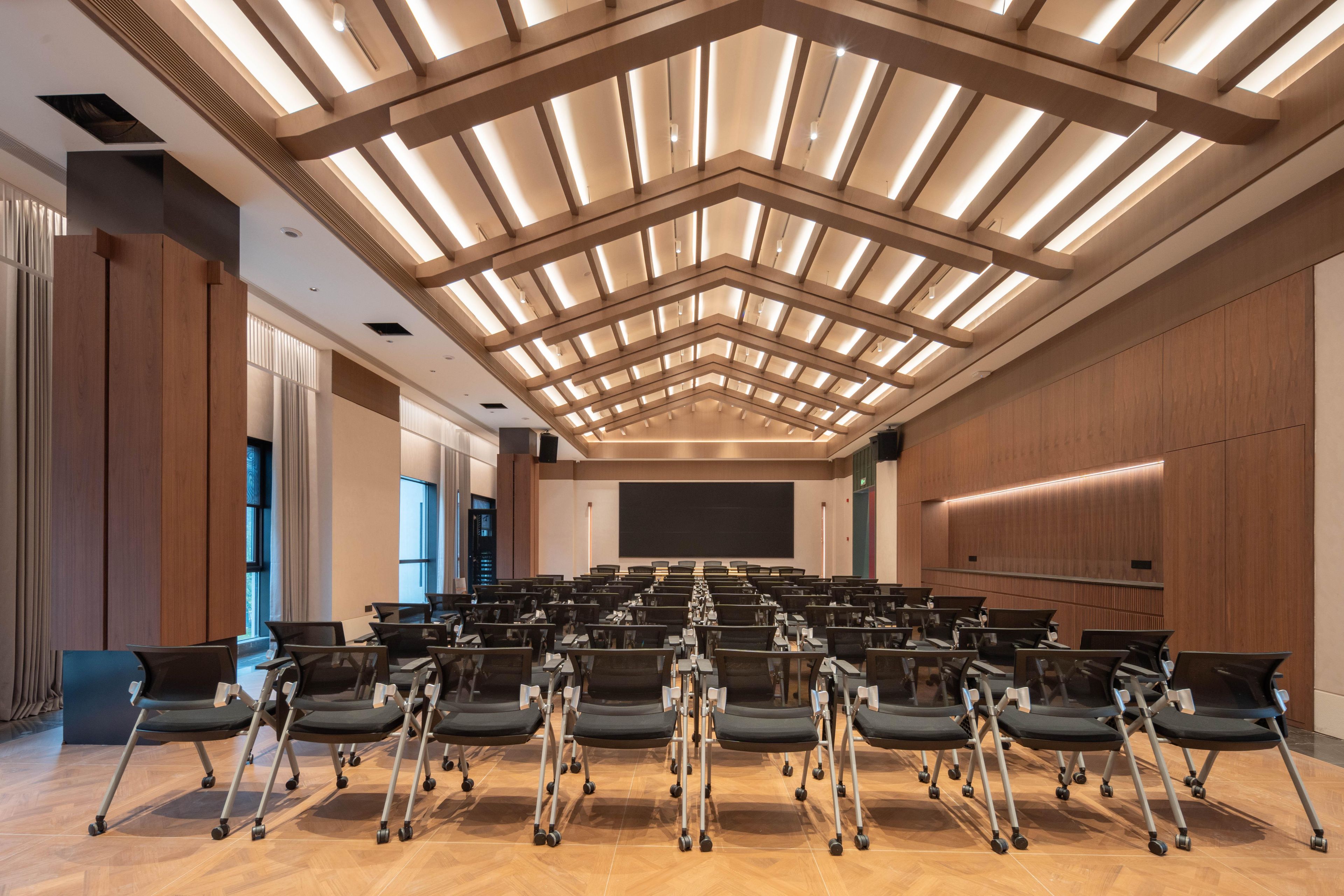 A conference room with rows of chairs, a large screen, and a modern ceiling design.