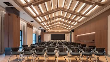 Un salón de conferencias con filas de sillas, una pantalla grande y un diseño moderno en el techo.