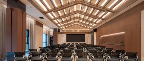 Une salle de conférence avec des rangées de chaises, un grand écran et un design moderne au niveau du plafond.