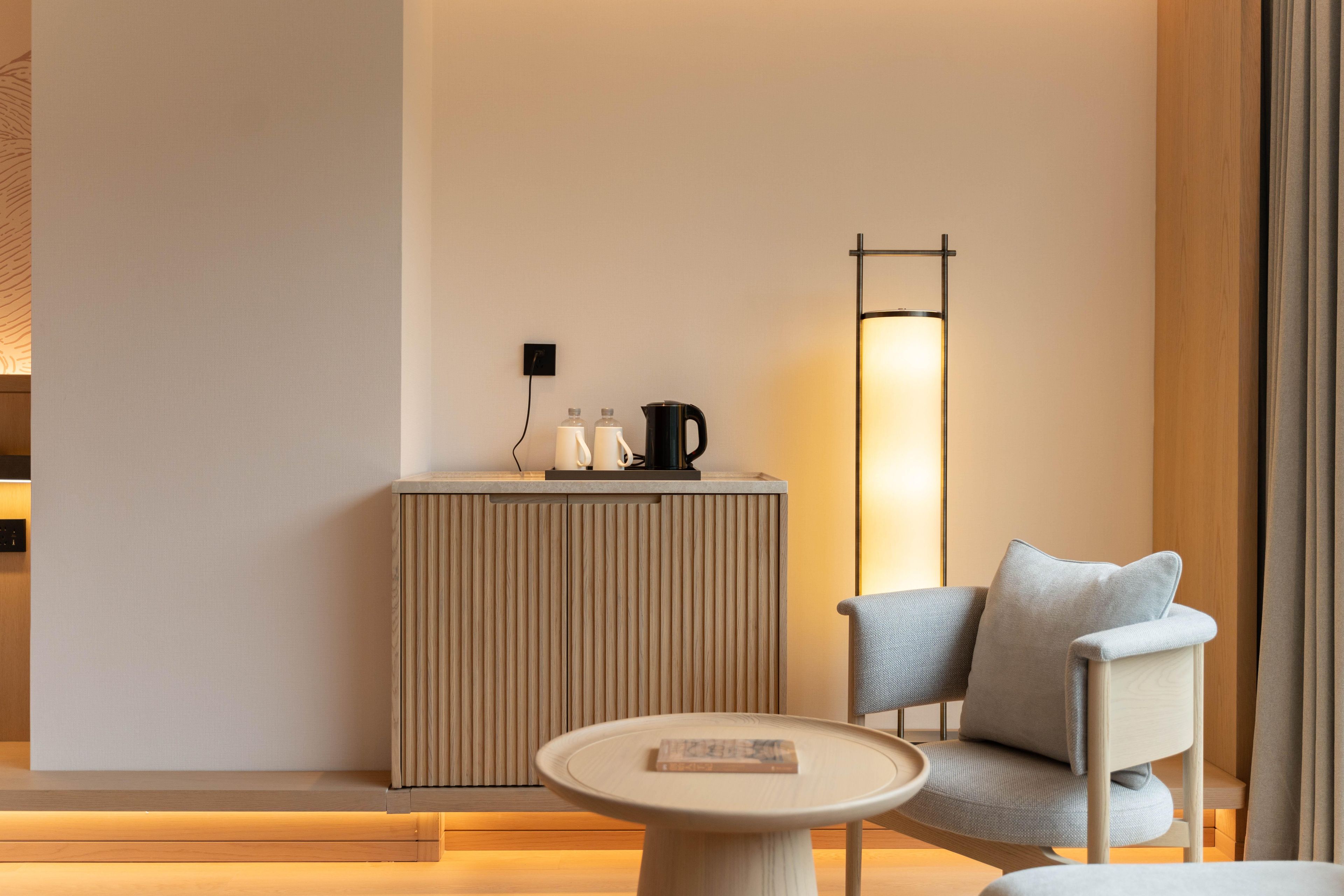 Una habitación moderna con una mesa redonda, un sofá, una lámpara de pie alta y un mueble pequeño con una tetera y tazas.