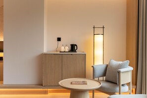A modern room with a round table, a sofa, a tall floor lamp, and a small cabinet with a kettle and cups.