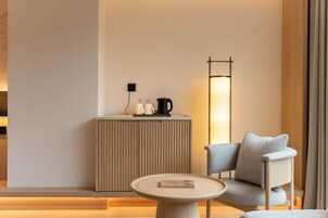 A modern room with a round table, a sofa, a tall floor lamp, and a small cabinet with a kettle and cups.