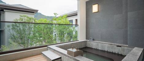 A modern spa area with a stone hot tub, wooden deck, and a view of surrounding buildings and trees.