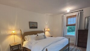 Un dormitorio con una cama grande, dos mesitas de noche con lámparas, una ventana con cortinas y un aparador de madera.