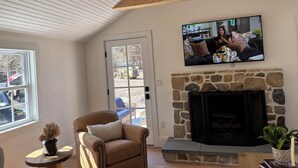 Una sala de estar con chimenea de piedra, televisor montado, sillón de cuero y vistas a través de un ventanal.