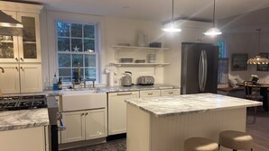 Una cocina moderna con armarios blancos, una isla de encimera de mármol, un refrigerador de acero inoxidable y un comedor con mesa y taburetes de bar.