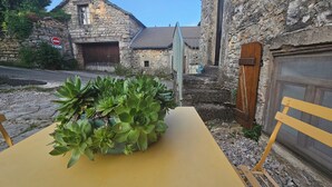 Een gele tafel met een vetplant in het midden, een stenen gebouw met een metalen poort, en een verboden toegang-bordje op de achtergrond.