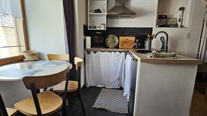 Een compacte keuken met een eethoek, met een klein kookeiland, een magnetron, waterkoker en koffiezetapparaat.