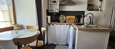 Uma cozinha compacta com área de refeições, com uma bancada pequena, micro-ondas, chaleira e cafeteira.