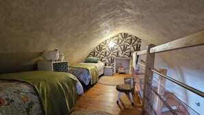 Een gezellige slaapkamer onder de dakpannen met twee bedden, een houten trapje en een kamer met een gedessineerd plafond.