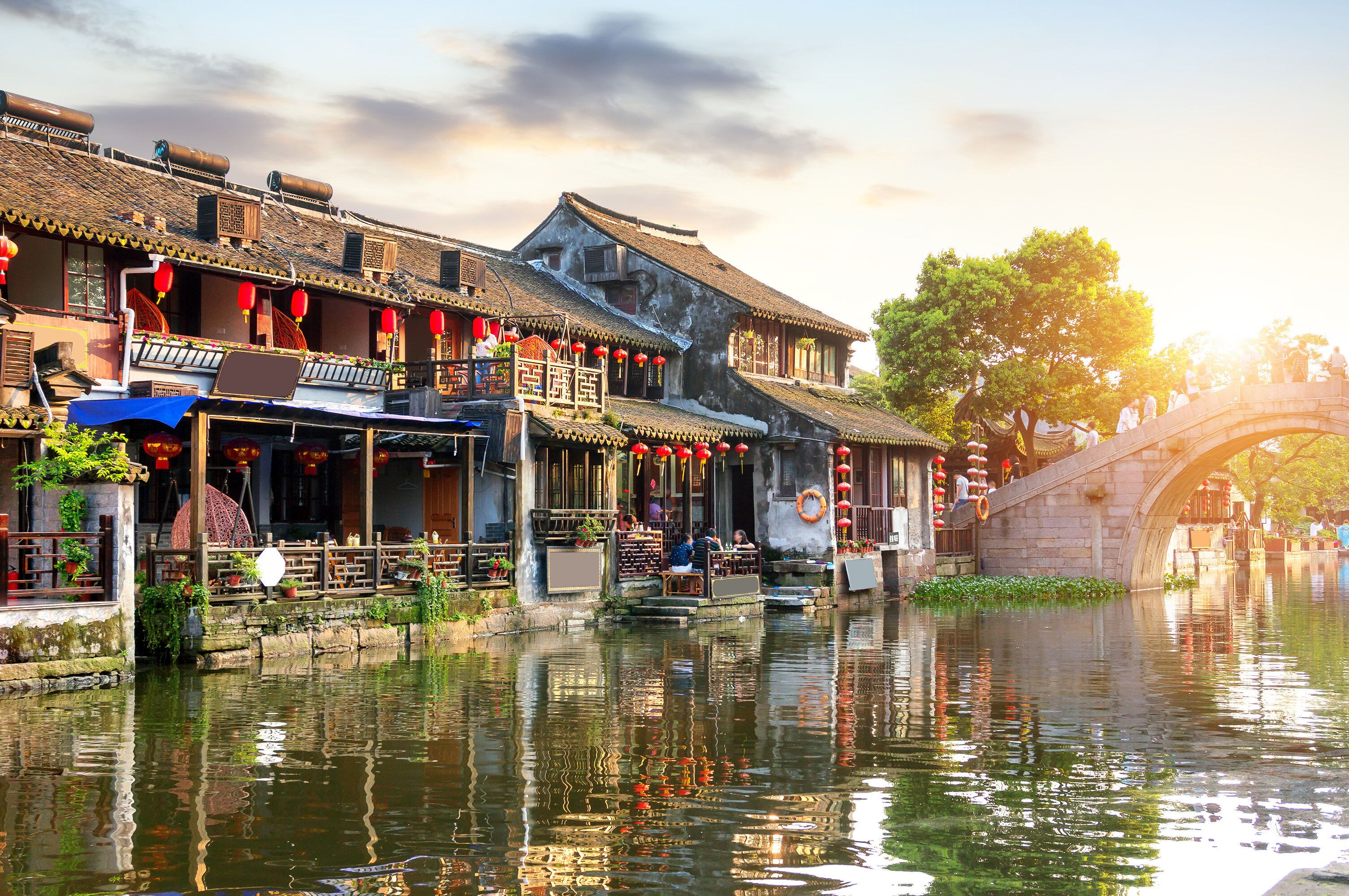 A traditional building with a tiled roof, a stone bridge, and a reflection in the water.