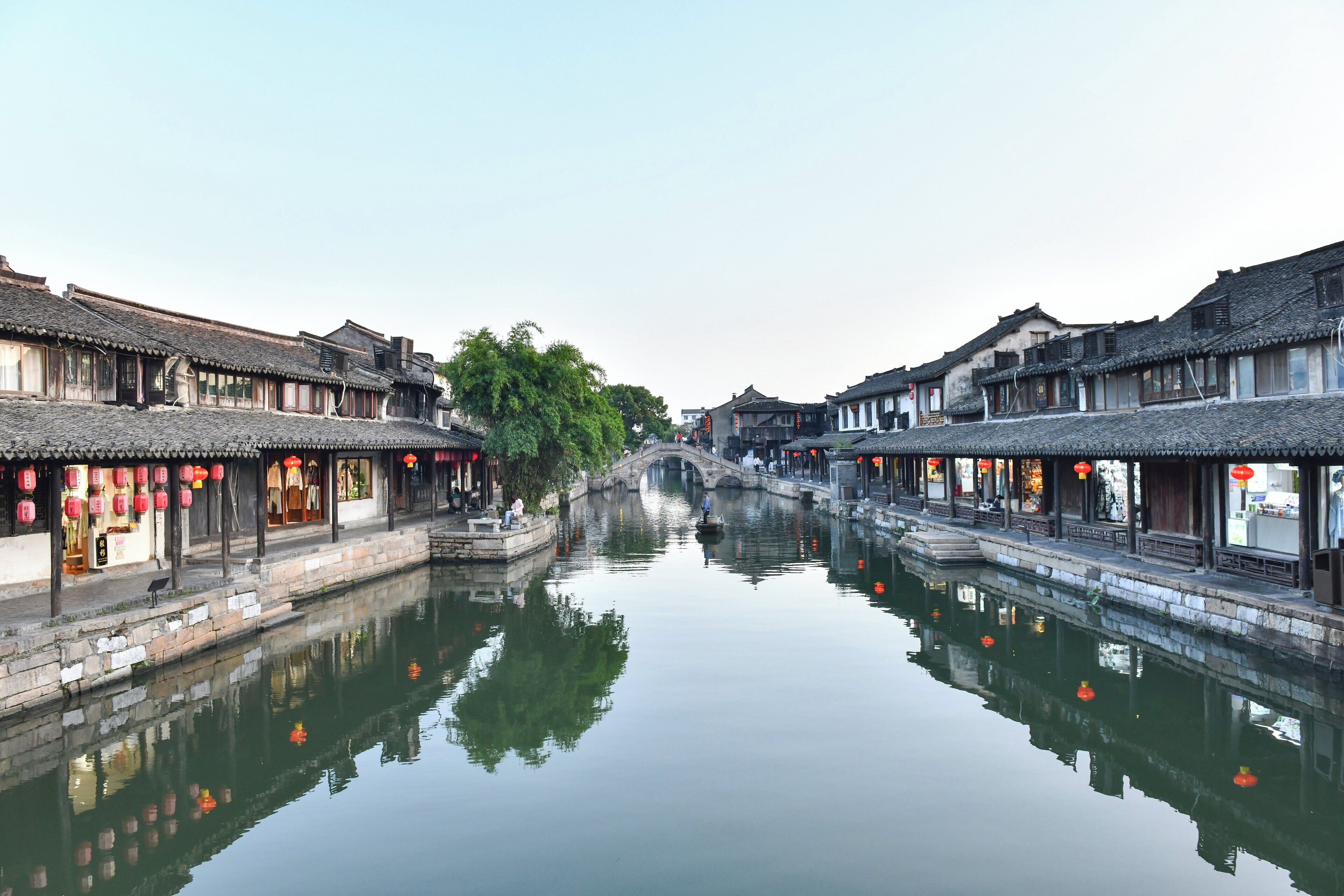 Ein traditioneller chinesischer Innenhof mit Wasserkanal, Steinbrücke und Holzbauten mit roten Laternen.