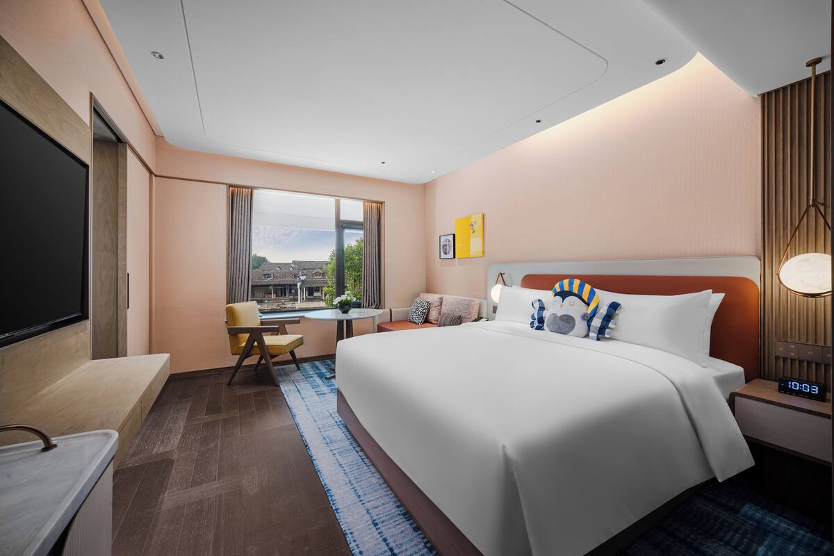 Ett modernt hotellrum med en stor säng, ett skrivbord, en stol och utsikt över stadsbilden genom fönstret.