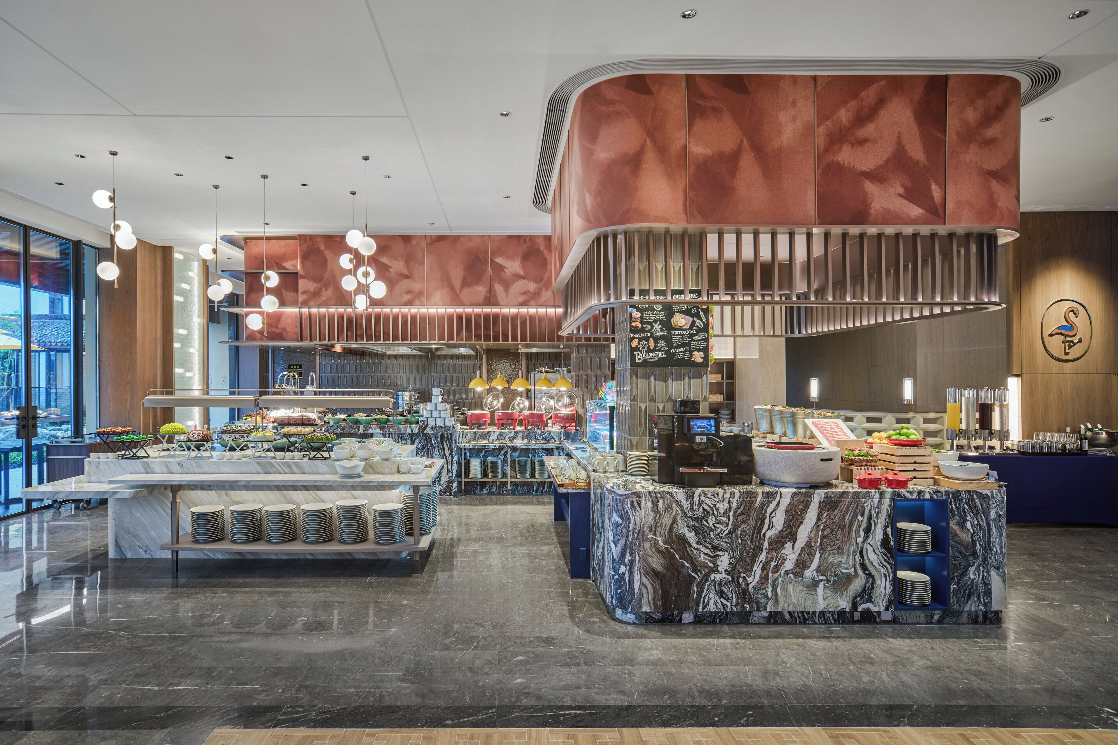 A modern buffet setup with marble counters, a variety of food items, and a large window offering a view of the city.