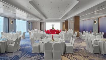 Une salle de banquet avec des tables rondes, des chaises blanches et un grand écran affichant du texte.