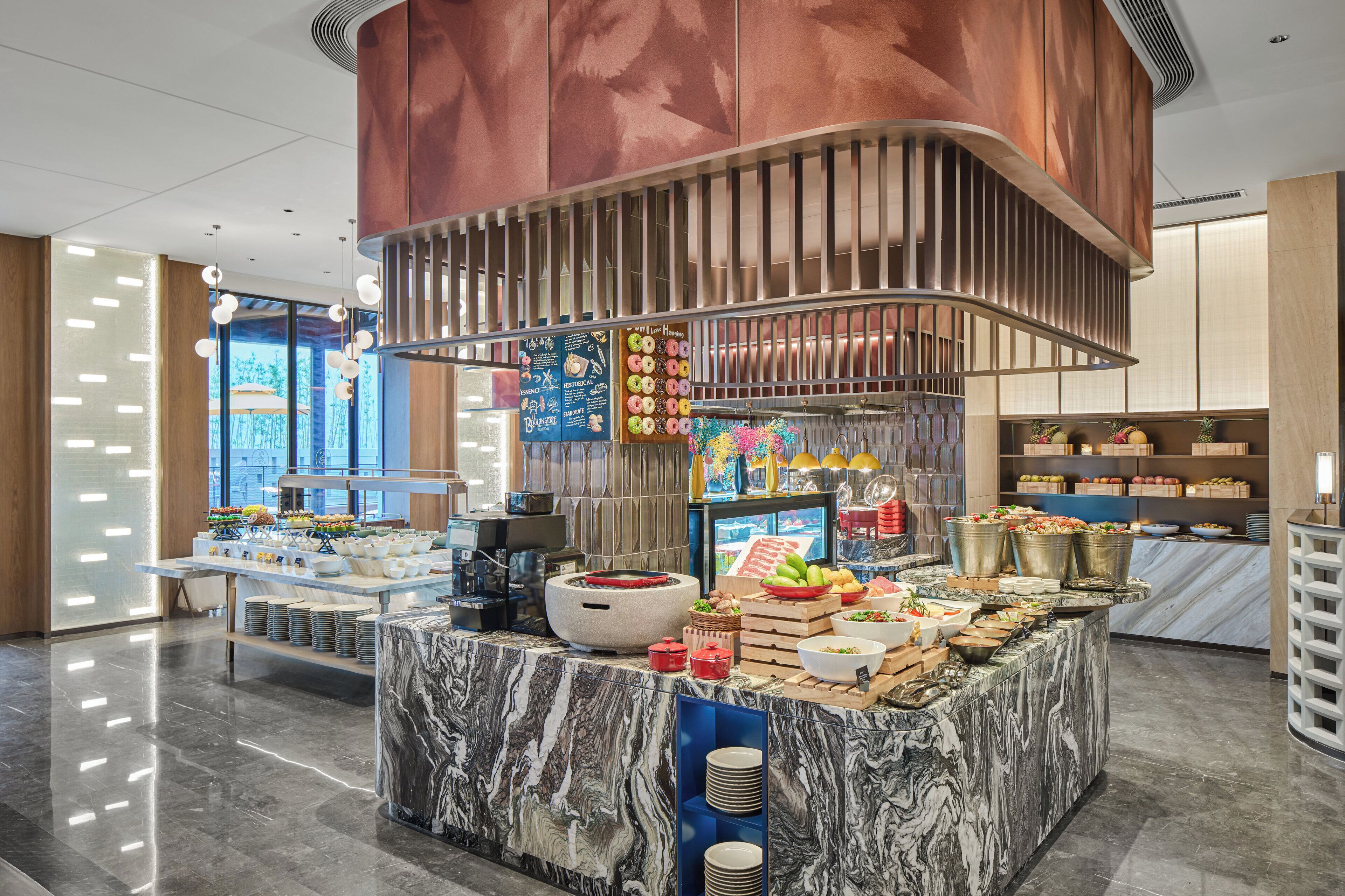 A buffet area with marble countertops, a variety of food items, and a modern design with a copper-colored structure.