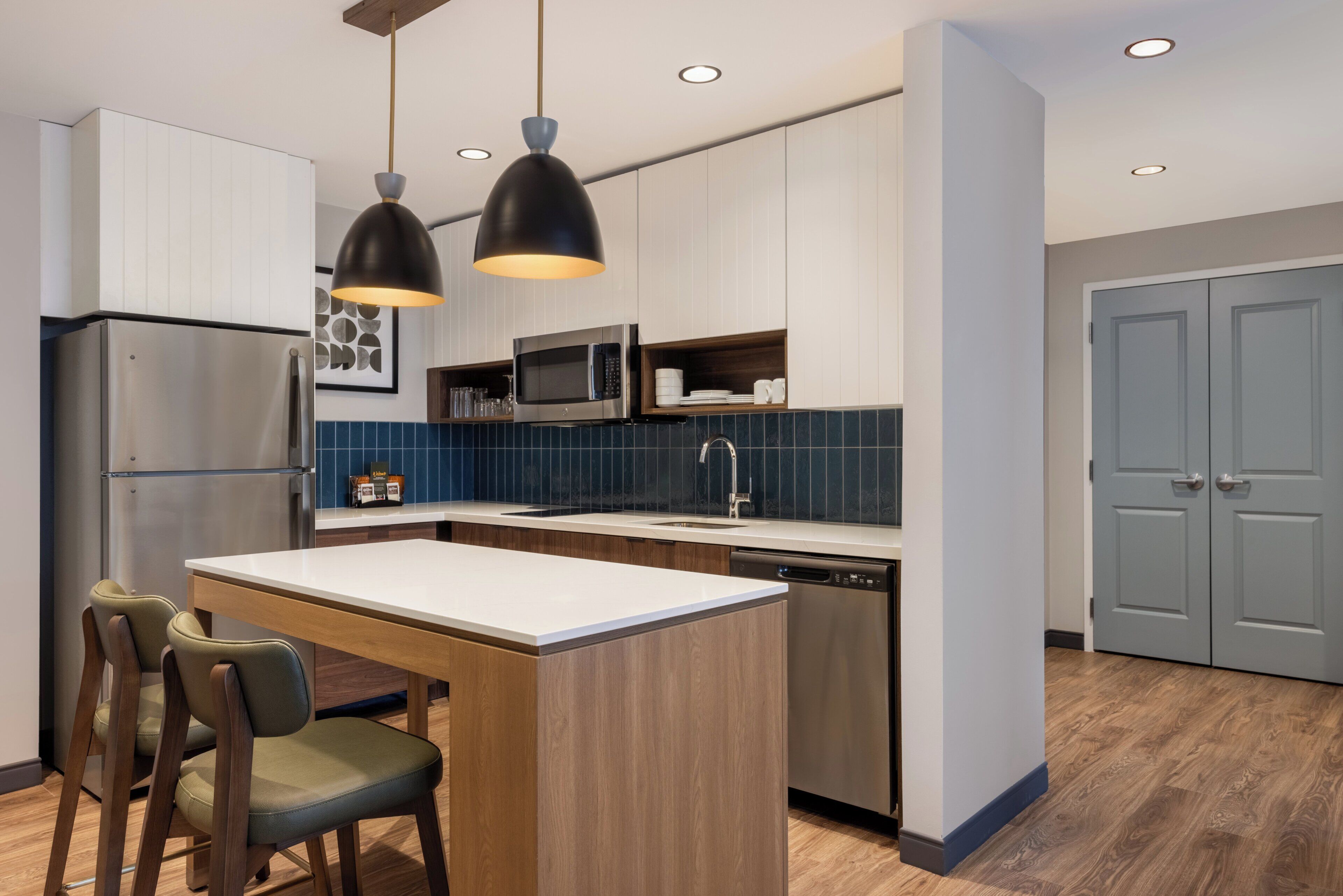 Une cuisine moderne dotée d’un îlot central, d’appareils électroménagers en acier inoxydable et de luminaires suspendus.