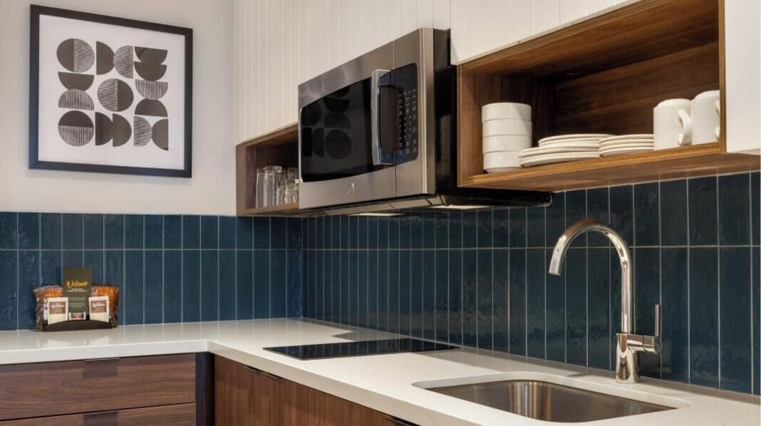 A kitchen with a microwave, sink, and wooden shelves with dishes.