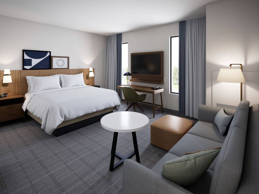 A modern hotel room with a bed, a desk, a TV, a sofa, and a small table.