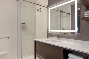 A modern bathroom with a glass shower enclosure, a white sink, a large mirror, and wooden cabinetry.