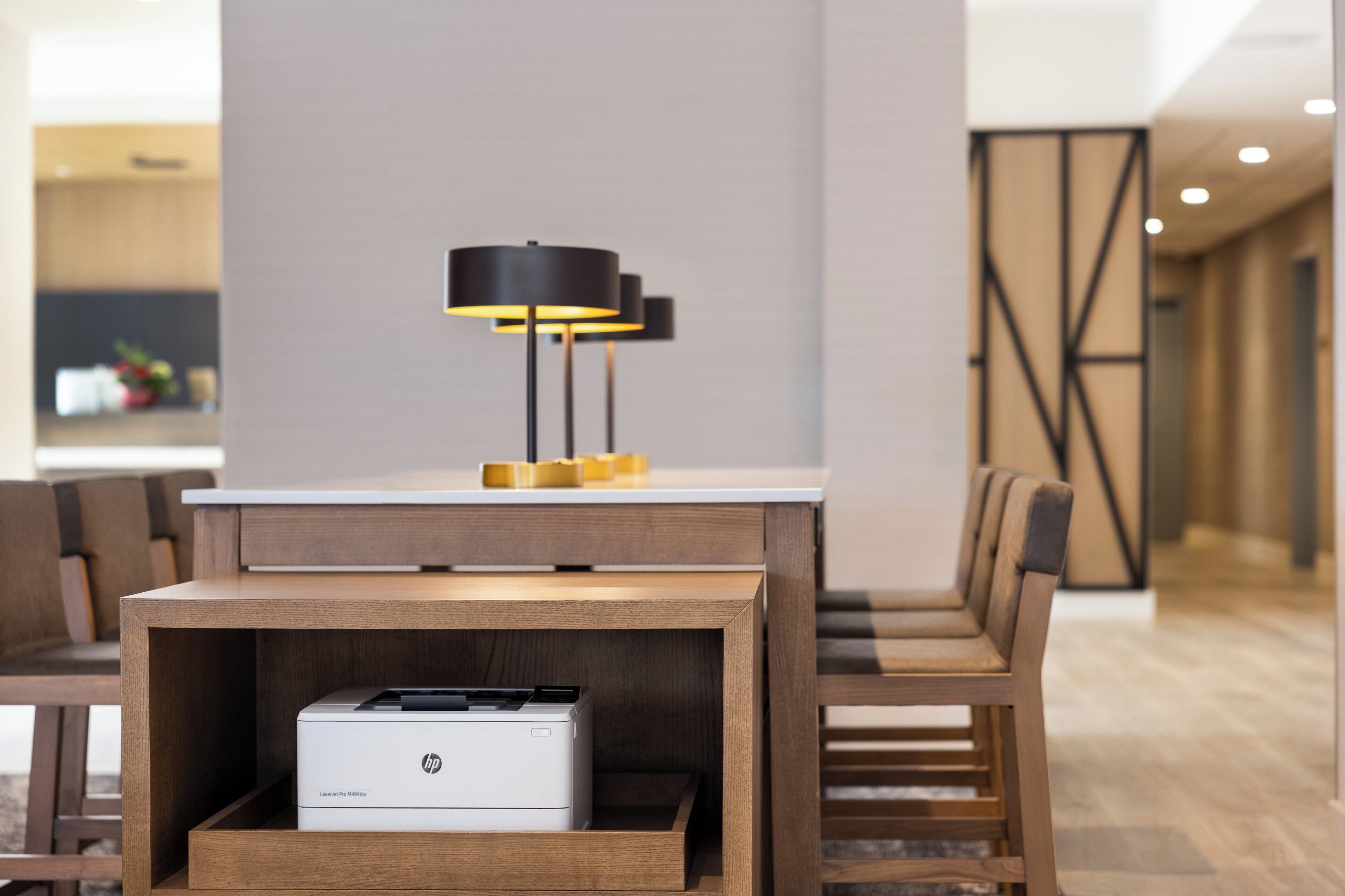 A modern hotel lobby with a wooden reception desk, a black floor lamp, and a printer drawer.