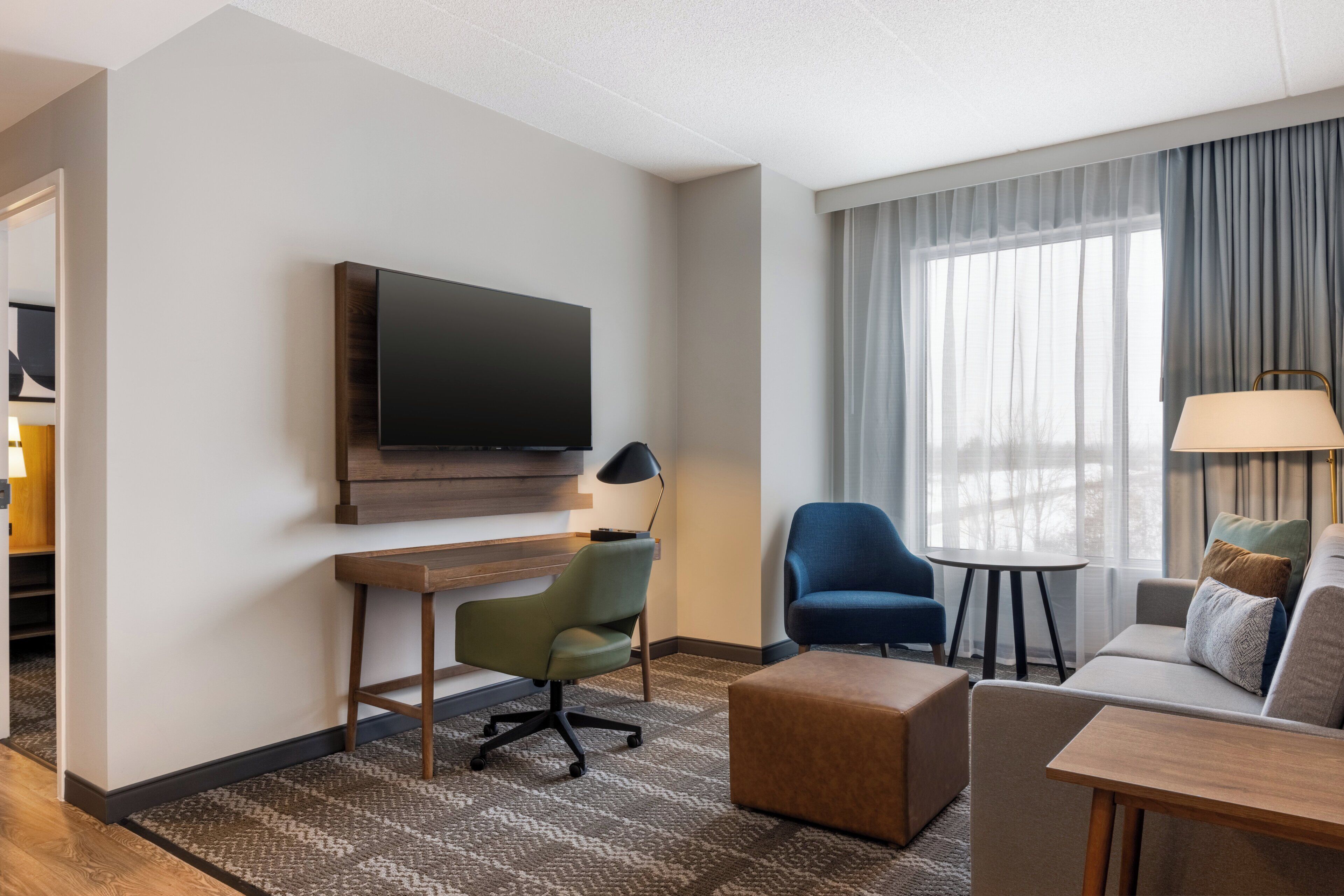 Habitación de hotel con televisión de pantalla plana, escritorio, un sillón azul, sofá y una mesita.