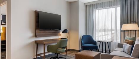 Habitación de hotel con televisión de pantalla plana, escritorio, un sillón azul, sofá y una mesita.