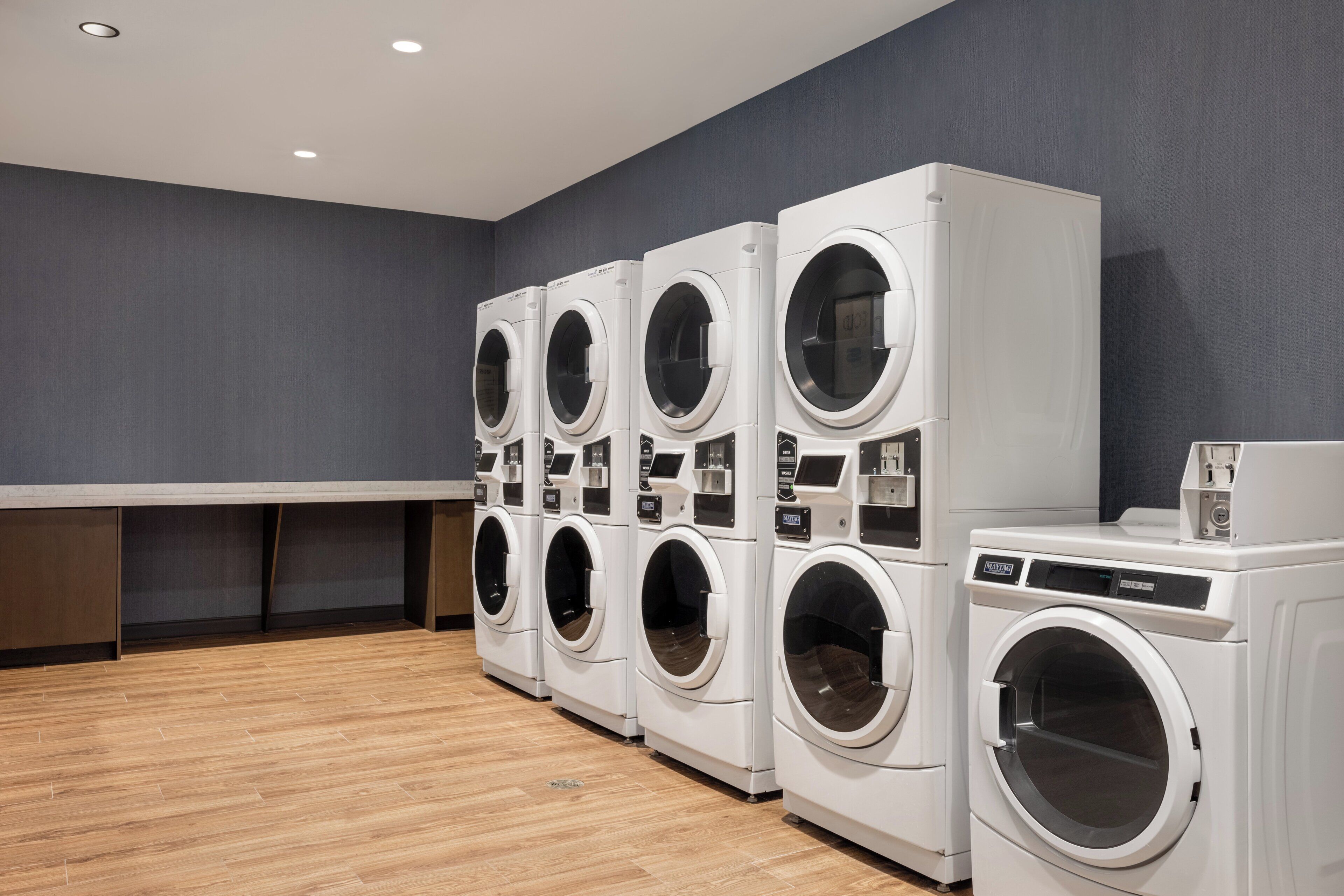 A laundry facility with multiple washing machines and dryers, wooden flooring, and a grey wall.