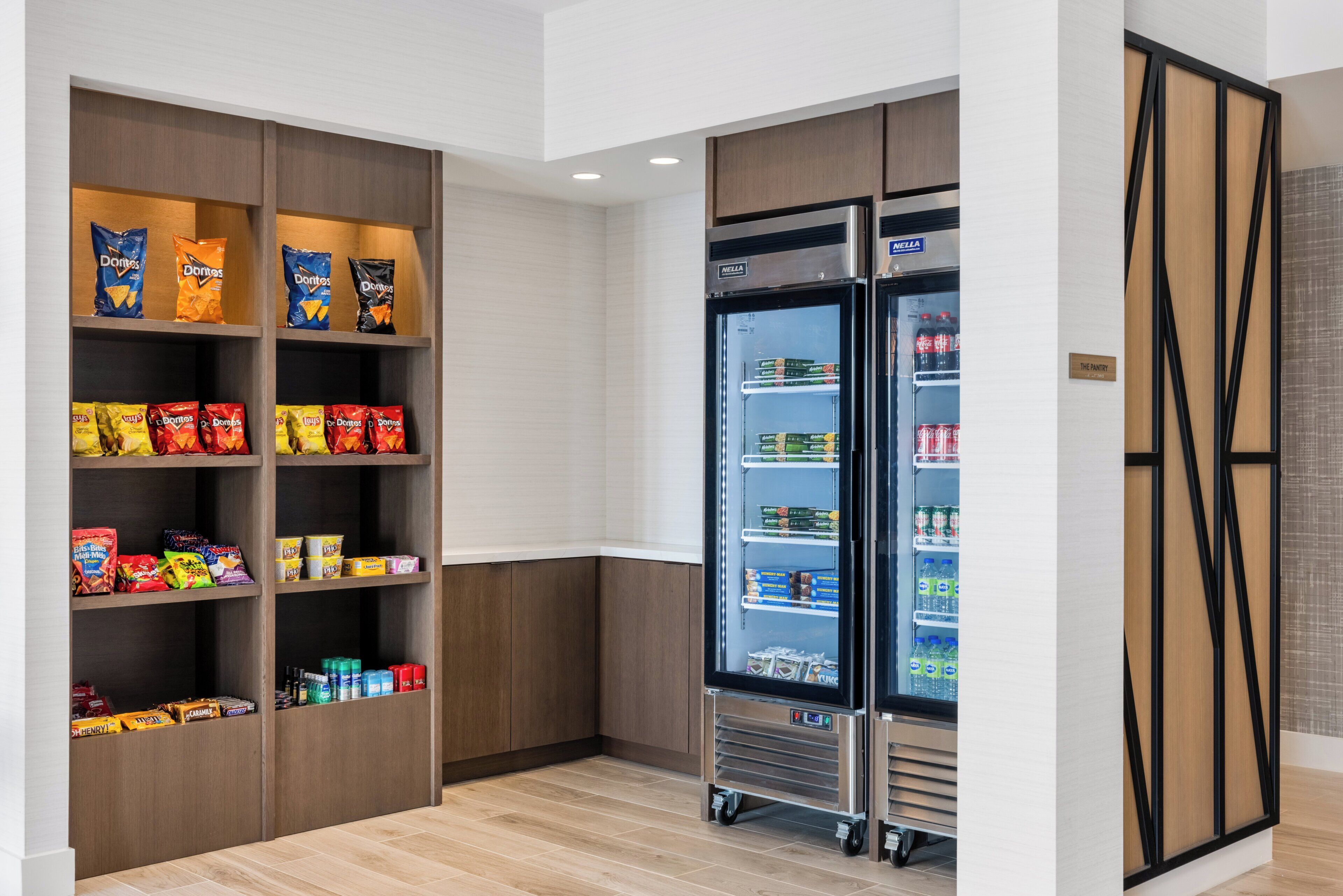Una despensa d'hotel amb estantes plenes d'aperitius i un refrigerador amb begudes.
