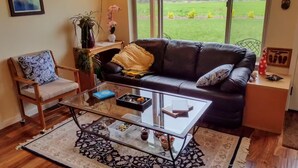 Un salon avec un canapé en cuir noir, une table basse en verre, une chaise en bois et une grande fenêtre donnant sur un champ verdoyant.