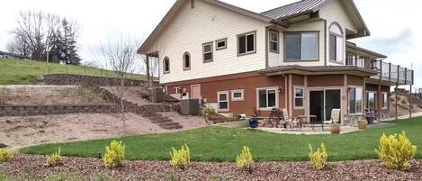 A two-story house with a large front porch, a covered patio, and a landscaped yard with young trees.