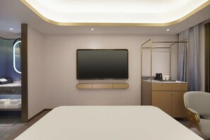 Una habitación de hotel moderna con una cama grande, un televisor de pantalla plana montado en la pared, un escritorio con una silla y un armario.