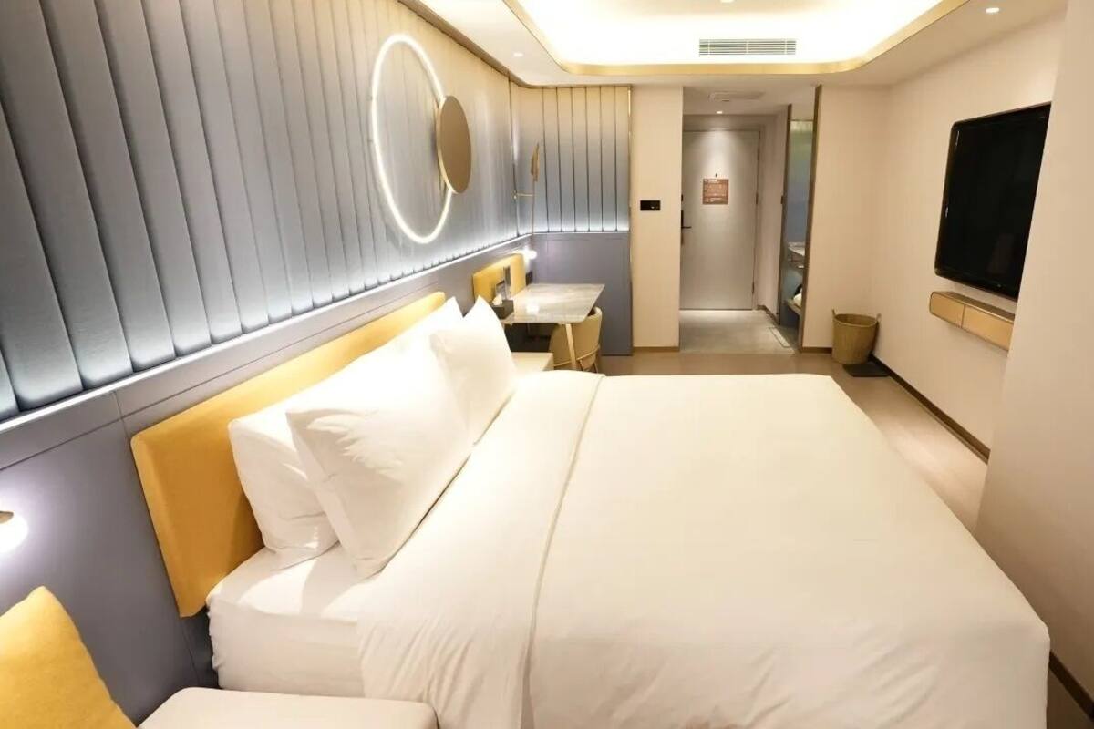 Habitación de hotel moderna con una cama grande, mesitas de noche, televisor y baño visible a través de una puerta abierta.