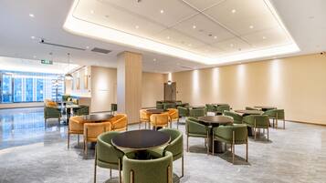 En modern hotellobby med en rymlig planlösning, flera sittgrupper och ett stort fönster med utsikt över staden.