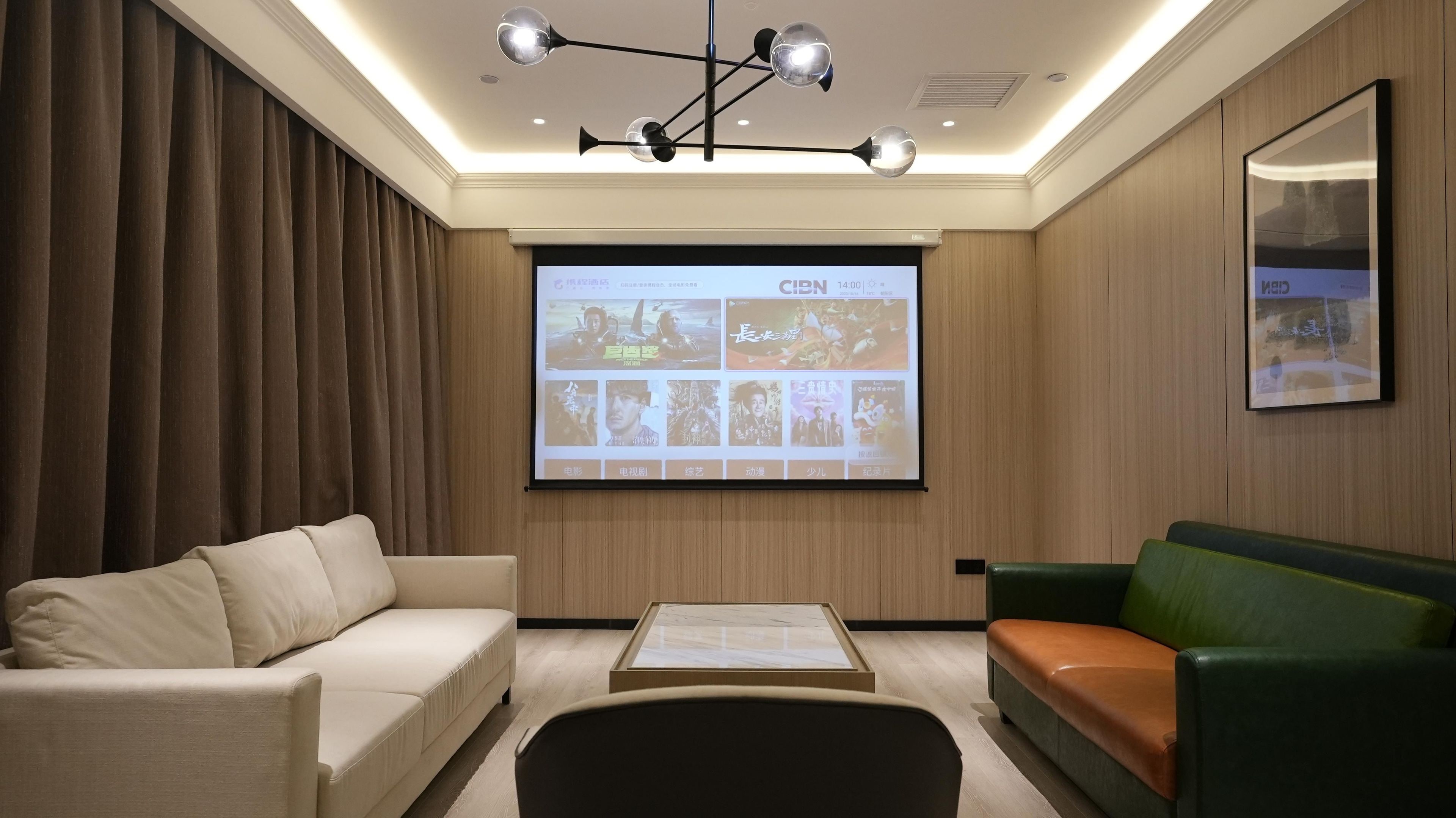 Una habitación moderna con una pantalla de proyección mostrando carteles de películas, un sofá, una mesa de centro y un sofá verde.