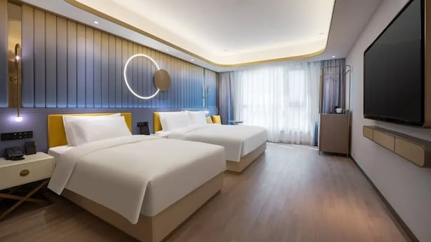 Et moderne hotelværelse med to senge, et fjernsyn, et sengebord og en rund lampe.