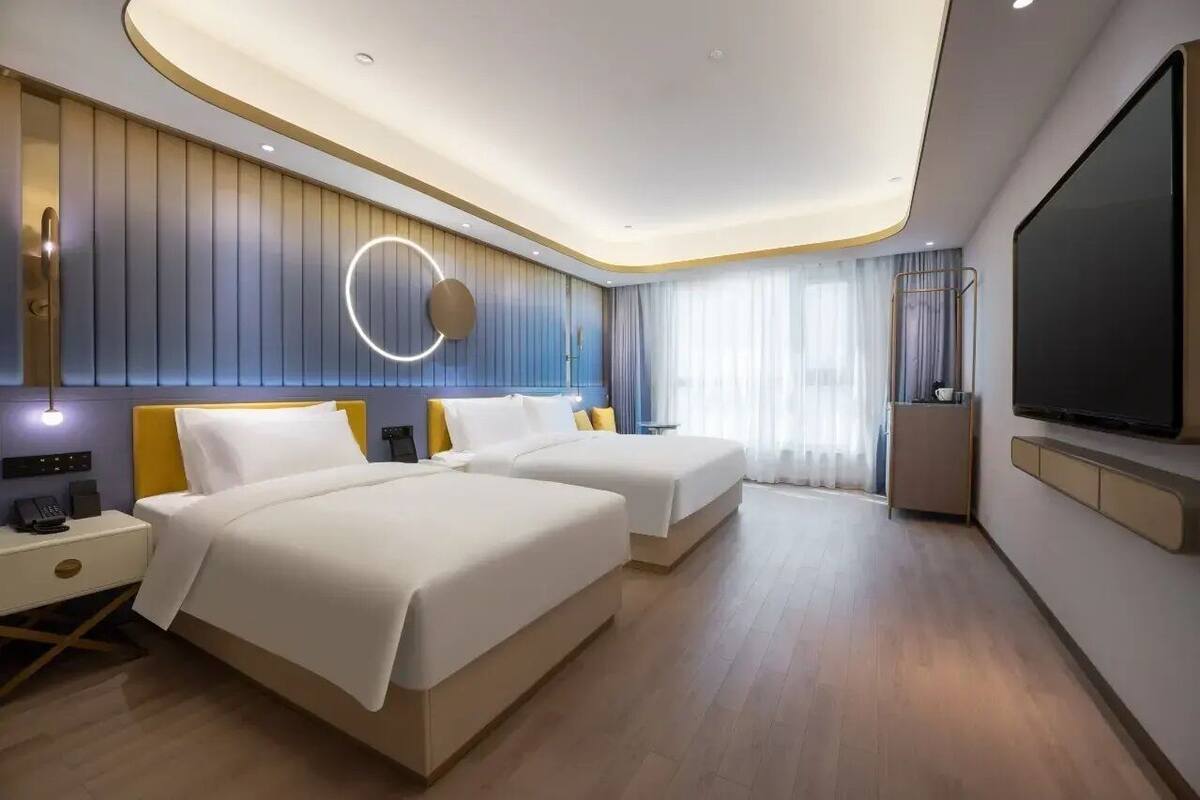 Una habitación de hotel moderna con dos camas, un televisor, una mesita de noche y una lámpara circular.