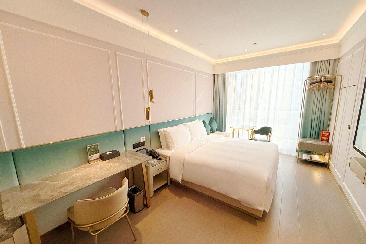 Habitación de hotel con cama, escritorio, silla, mesita, espejo y armario.