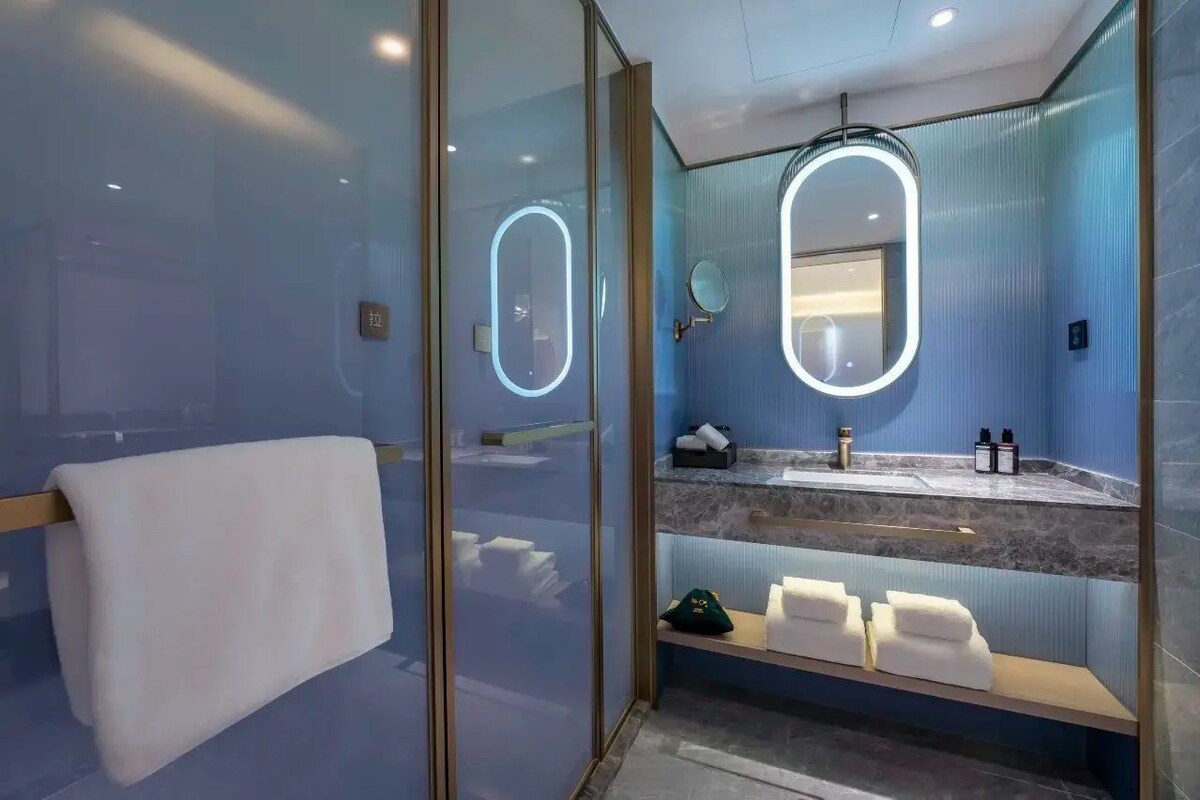 Un baño moderno con cabina de ducha de vidrio, tocador con encimera de mármol y barra para toallas.