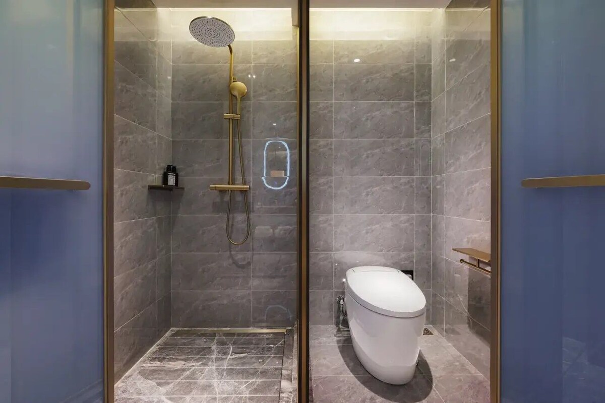 Ein modernes Badezimmer mit einer gläsernen Duschkabine, Toilette und Marmorboden.