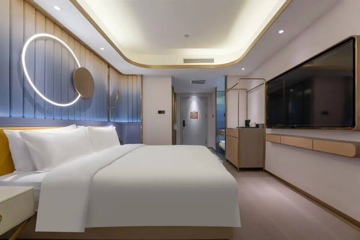 Habitación de hotel moderna con una cama grande, televisor, minibar y una lámpara circular en la pared.