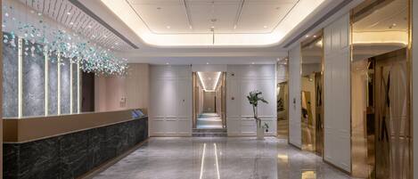 A hotel lobby with a marble reception desk, a long corridor, and a modern ceiling design.