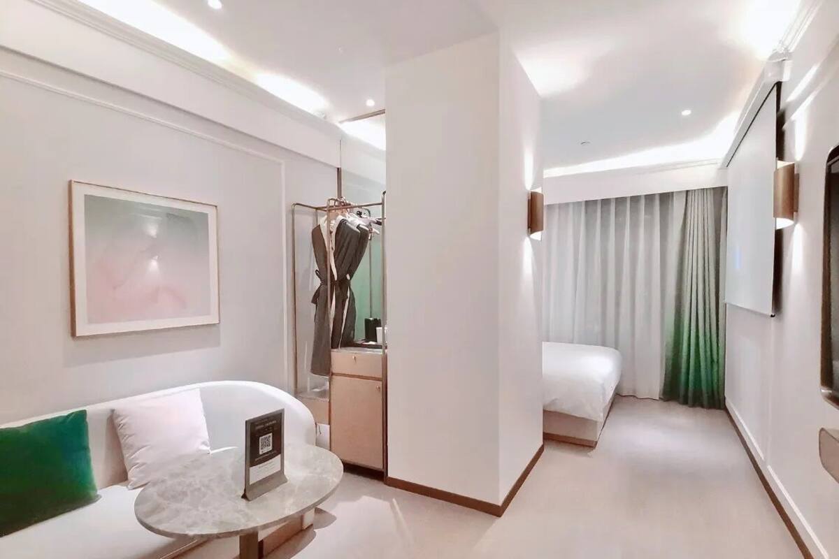 Una habitación de hotel moderna con sofá, una mesita redonda, cama, armario y espejo.